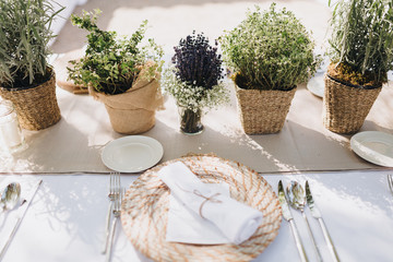 on festive table in wedding banquet area are plates, glasses, candles, cutlery, the table is decorated with compositions from greens and napkins