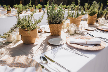 on festive table in wedding banquet area are plates, glasses, candles, cutlery, the table is decorated with compositions from greens and napkins