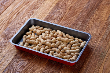 Unpeeled raw peanut on baking tray over wooden background, selective focus, shallow depth of field.