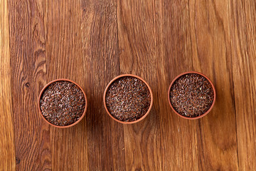 Flax seeds in wooden bowl on rustic wooden background, top view, selective focus