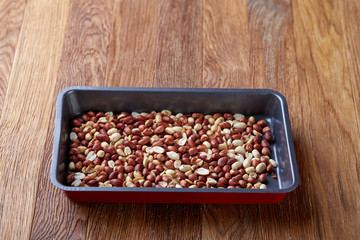 Mix of peeled raw peanut on baking tray over wooden background, selective focus, shallow depth of field.