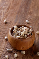 Fototapeta na wymiar Salted pistachios on a wooden plate over wooden background, top view, close-up, selective focus.