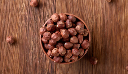 Hazelnuts in overturned ceramic bowl on wooden background with copy space, top view, selective focus.