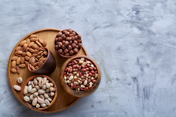 Mixed nuts in brown bowls on wooden tray over white background, close-up, top view, selective focus.