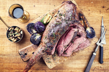Marinated barbecue aged leg of venison with mushrooms and red cabbage as top view on a rustic board
