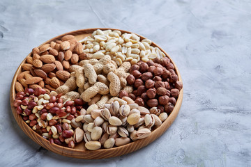 Mixed nuts in brown bowls on wooden tray over white background, close-up, top view, selective focus.