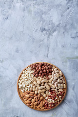 Mixed nuts in brown bowls on wooden tray over white background, close-up, top view, selective focus.