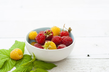 red and rare yellow raspberry fruits on white wooden table background