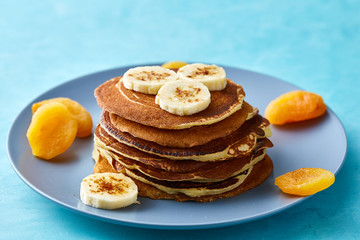 Pile of homemade pancakes with banana and walnuts on blue background, selective focus