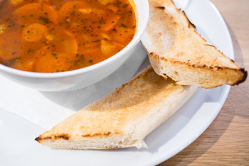 Light and tasty soup on white plate with pastry detail, Spring soup with fried baguette, Vegetable soup with baguette on wooden table
