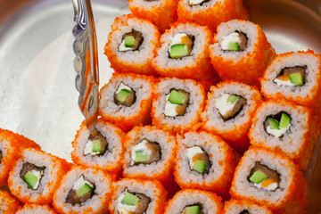 View of a Philadelphia roll sushi on a counter in supermarket and a fragment of metal kitchen tongs