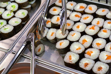 View of a rolls sushi in black soy paper on a counter in supermarket and metal kitchen tongs