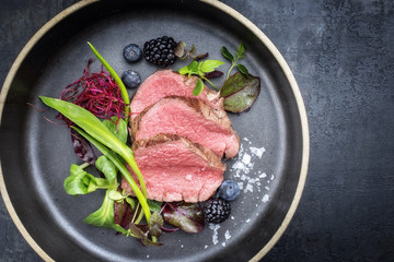 Traditional barbecue aged sliced fillet steak with wild garlic and fruits top view on a plate with copy space