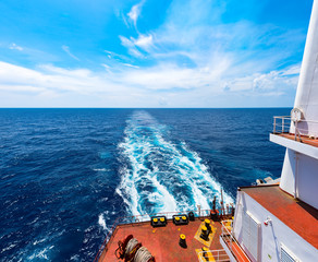 Panoramic view on trail on sea surface behind cargo ship at sea in beautiful sunny day