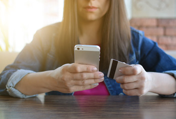 A brunette girl in a denim jacket is eating lunch in a cafe and using her phone. Communication through messenger. Smartphone. Casual loose clothing.