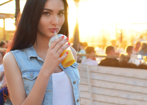 Healthy lifestyle. The brunette girl drinks fresh juice through a straw. Widely open eyes. Orange fresh. Vitamins. Surprise. Close-up portrait. Delicious.