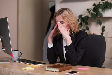 Businesswoman closed face with hands by sitting at desk. Tired after work.