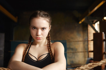 Fototapeta na wymiar People, youth, sports, leisure, hobby and active lifestyle concept. Picture of self determined young muscular woman wearing black top staring at camera with serious look, resting during workout