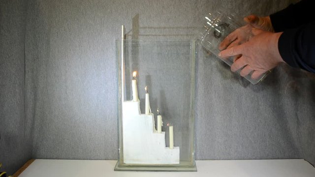 Carbondioxide (CO2) is poured from a large glass into another glass with 4 candles. Even if it seems that nothing is poured, the candles go out one by one starting from the bottom.