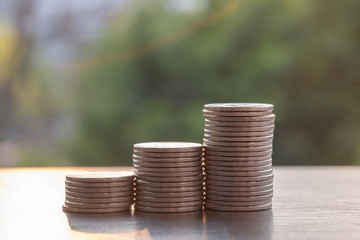Money saving concept. Close up of stack of silver coins on wooden table with sunlight.