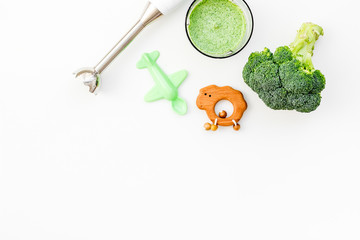 Homemade baby food. Cook puree with broccoli with immersion blender. White background with toy top...