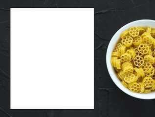 Macaroni ruote Pasta in a white bowl on a black textured background from the side. Close-up with the top. White space for text and ideas.