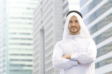 Bearded Arab (Islam) businessman wearing traditional dress, smiling face and standing for waiting partner to sign energy or oil contract with city background. Successful business partnership agreement