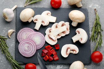 Sliced champignons, onions and red peppers on black cutting board