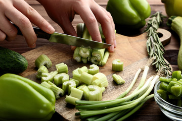 Female hand cutting fresh celeries on brown board