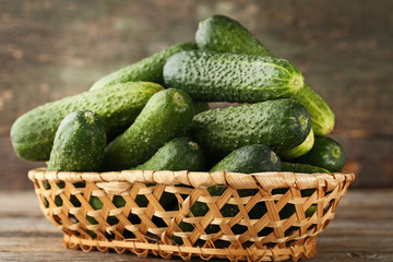 Fresh cucumbers in basket on grey wooden table