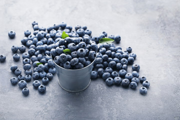 Ripe blueberries in bucket on grey wooden table