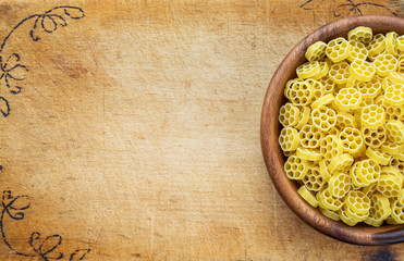 Macaroni ruote pasta in a wooden bowl on a cutting wooden board, texture background with a side. Close-up with the top. Free space for text.