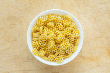 Macaroni ruote pasta in a white cup on a wooden table textured background, in the center close-up with the top.