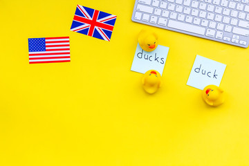 Teach english to a child. Funny english. British and american flags, computer keyboard, stickers with vocabulary, toy duck on yellow background top view copy space