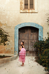 Fototapeta na wymiar a girl in a fairy dress of a princess with a crown turns around walkng to the door of an ancient castle house