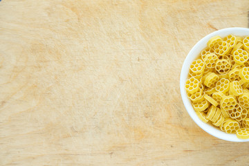 Macaroni ruote pasta in a white bowl on a wooden table textured background with a side. Close-up with the top. Free space for text.