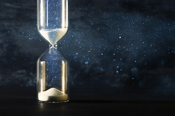 Image of hourglass as time passing concept over black background for business deadline. Glitter...