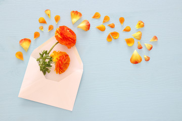 Image of envelope with delicate pastel orange and yellow beautiful flowers arrangement over blue wooden background. Flat lay, top view.