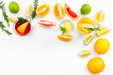 Concept of alcoholic cocktail with fruits. Glass with beverage near oranges, grapefruit, lime and rosemary on white background top view copy space