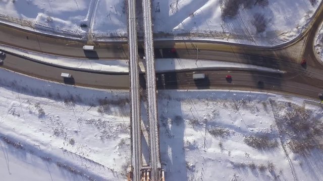 Cars and cargo trucks moving on winter highway under train bridge drone view. Car traffic on snowy road on winter landscape. Aerial view suspension railway bridge over highway road.