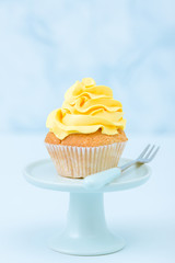 Cupcake with yellow cream decoration on vintage stand on blue pastel background. Minimalist concept in food.
