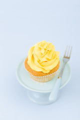 Cupcake with yellow cream decoration on vintage stand on blue pastel background. Minimalist concept in food.