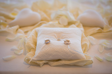 Wedding rings together with white rope on white pillow surrounded white hearts. Marriage ceremony