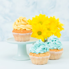 Cupcake with sweet yellow cream decoration and bouquet of yellow chrysanthemum in retro shabby chic vase on blue pastel background.