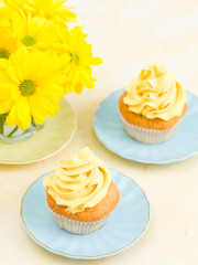 Cupcake with yellow cream decoration and bouquet of yellow chrysanthemum in small glass.