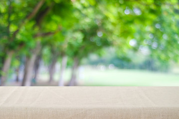 Empty table with brown linen tablecloth over blurred park nature background, for product display montage, spring and summer