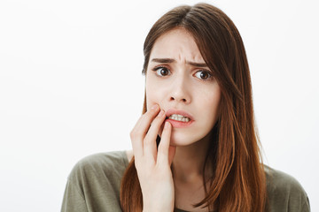 Oops, she answered wrong during test. Indoor shot of displeased troubled girl, frowning and looking upset while worrying about issue, holding hand near mouth, standing over gray background