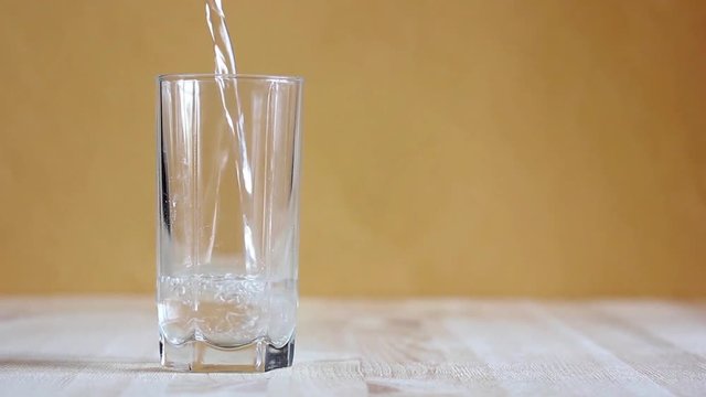Clean water flows into an empty glass standing on a wooden table.