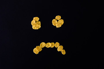 Sad face smiley from cornflakes on a black background