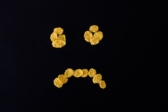 Sad face smiley from cornflakes on a black background - Powered by Adobe
